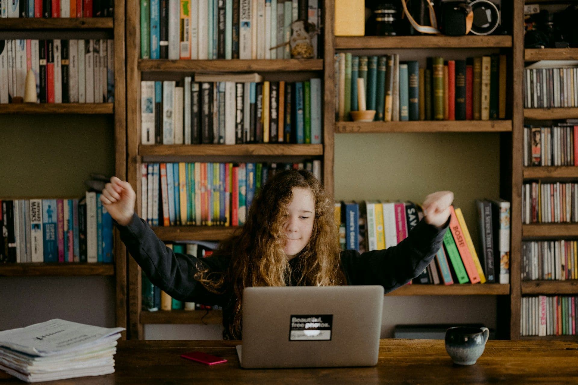 Girl sat in front of bookcase, on her laptop.